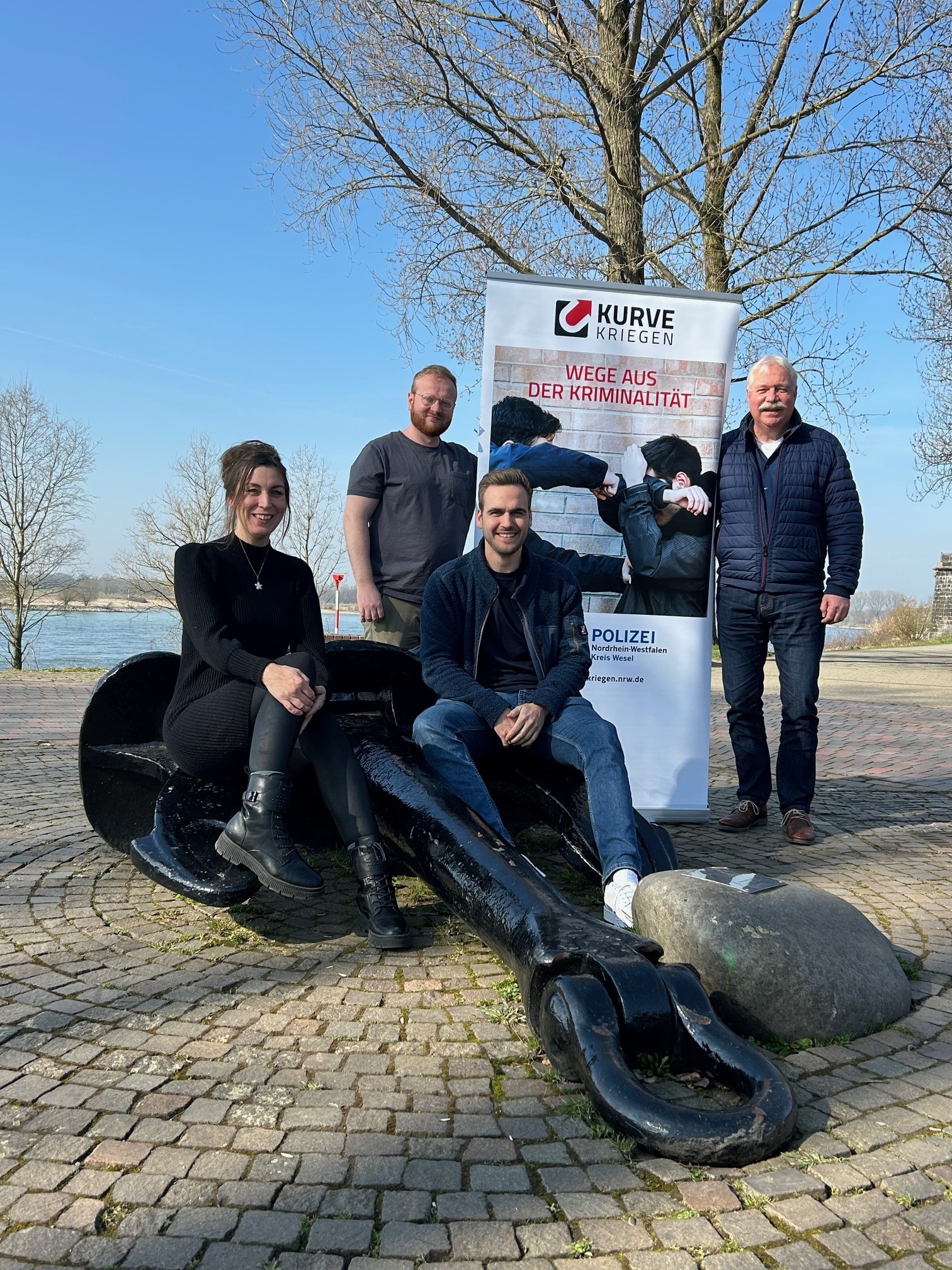 Kurve kriegen Team Wesel - eine Frau und 3 Männer sitzen und stehen vor einem Kurve kriegen Banner